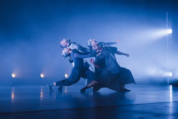 Cuatro bailarines en escena con movimientos enérgicos y fluidos, representando un proceso de cambio y disolución de la identidad.