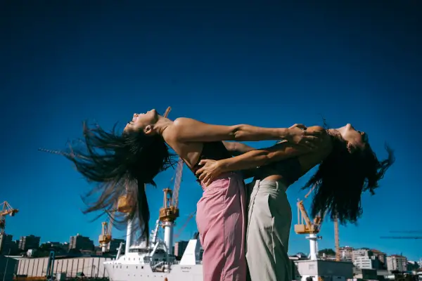 Dos bailarinas en un escenario al aire libre, con movimientos que expresan conexión y apoyo mutuo entre mujeres.