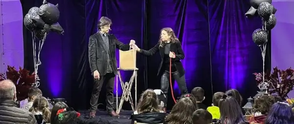 Dos ilusionistas, Martín Camina y Maga Fani, en el escenario con un fondo oscuro, realizando un truco de magia.
