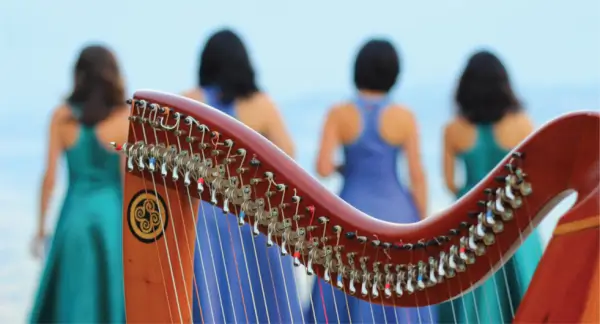 Cuatro mujeres del grupo Lulavai tocando arpas celtas y cantando en un escenario iluminado.