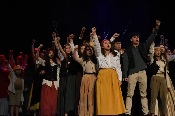 Escena del musical 'Miserábeis' con un gran elenco de estudiantes y profesores del IES Isla de Ons en el Salón Teatro, con vestuario de época.