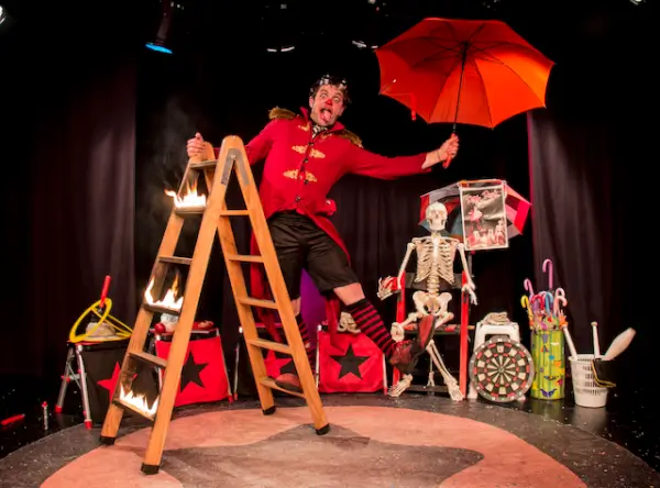 Peter Punk Pallaso realizando un acto de equilibrio con paraguas en un escenario de circo.