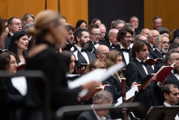 Un coro juvenil cantando con entusiasmo en el escenario, acompañado por una orquesta sinfónica, con imágenes de películas proyectadas de fondo.